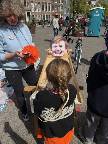 A child looks at a large portrait on a wooden stand while an adult stands nearby on a sunny street